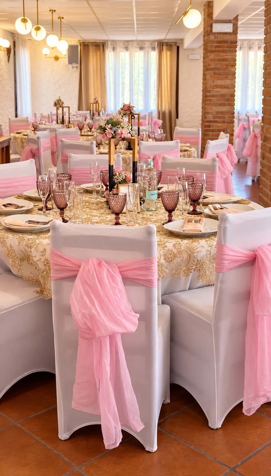 Sillas vestidas con lazos rosas alrededor de una mesa con mantel dorado